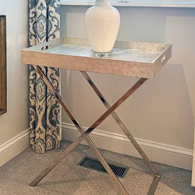 Sale Photo Thumbnail #198: Contemporary tray-top side table with a polished chrome X-frame base and removable metallic silver tray, topped with a white urn-shaped table lamp.