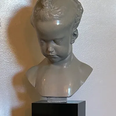 Sale Photo Thumbnail #184: Glazed ceramic bust sculpture depicting a young girl with braided hair, mounted on a polished black plinth base.