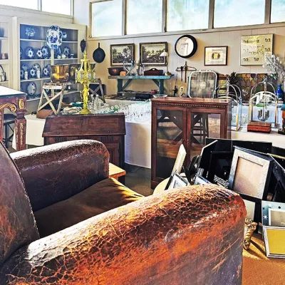 Sale Photo Thumbnail #277: Wide view of an estate sale room featuring a distressed leather armchair, vintage picture frames, small cabinets, and shelves of ceramic and glassware.