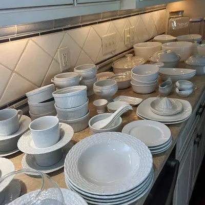 Sale Photo Thumbnail #45: Large collection of white ceramic kitchenware, including bowls, ramekins, saucers, and serving pieces arranged on a countertop.