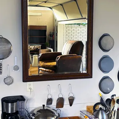 Sale Photo Thumbnail #262: Large rectangular wall mirror with a bevel-edged mirror glass and a dark stained wood frame, mounted above a table of kitchenware.