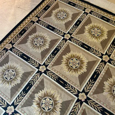 Sale Photo Thumbnail #193: Large area rug featuring a grid pattern of geometric squares and floral medallions in neutral tan, beige, and black tones.