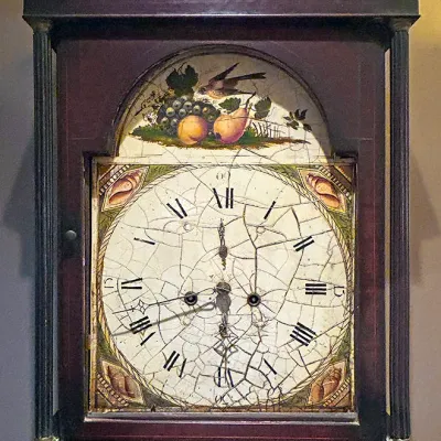 Sale Photo Thumbnail #100: Antique wooden grandfather clock featuring a painted dial with a bird and fruit motif, Roman numerals, and heavy crazing on the clock face.
