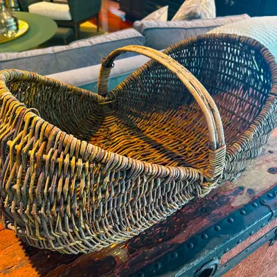 Sale Photo Thumbnail #99: Vintage woven wicker gather basket with an arched bentwood handle, sitting atop a distressed antique trunk.