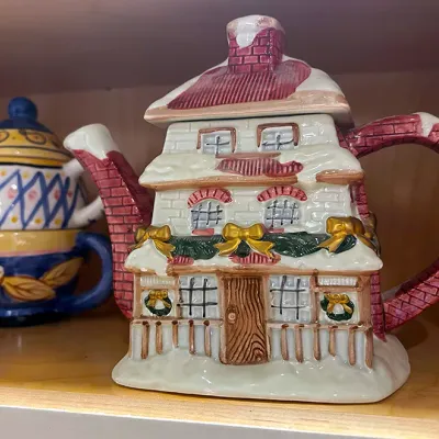 Sale Photo Thumbnail #91: Novelty ceramic cottage teapot with snow-covered roof and Christmas garland details, alongside a colorful hand-painted tea-for-one set.