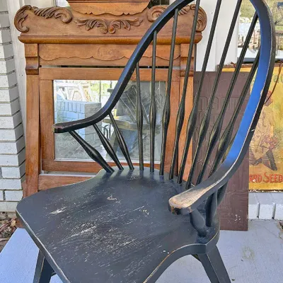 Sale Photo Thumbnail #251: Black painted Windsor-style armchair with distressed finish, positioned in front of a vintage carved wooden mirror frame.