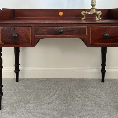 Sale Photo Thumbnail #207: Antique Federal-style mahogany writing desk featuring inlaid wood details, three drawers, turned legs, and a gallery top with side scrolls.
