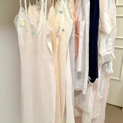 Sale Photo Thumbnail #2: Collection of vintage women's full slips and nightgowns hanging in a closet, featuring lace trim and embroidered floral details.