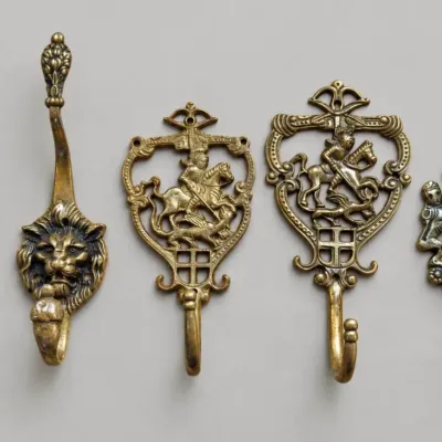 Sale Photo Thumbnail #92: Set of five vintage ornate brass wall hooks featuring lion heads, mounted knights, and heraldic coat of arms motifs.