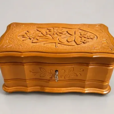 Sale Photo Thumbnail #95: Hand-carved Swiss wooden music box featuring intricate floral edelweiss details on the lid and a keylock front.
