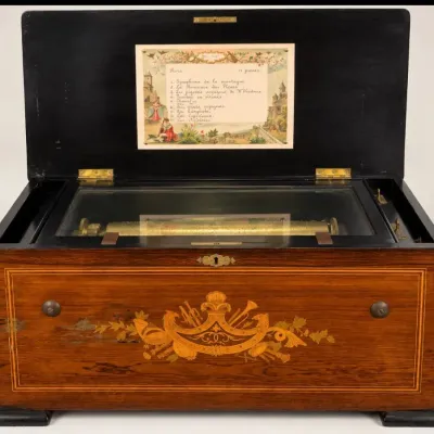 Sale Photo Thumbnail #78: Antique Swiss cylinder music box in a marquetry-inlaid wood case, featuring a handwritten song card under the lid listing 11 tunes.