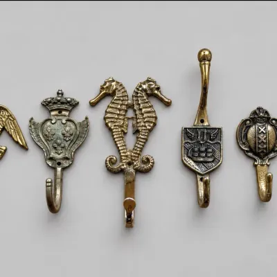 Sale Photo Thumbnail #57: Collection of six vintage cast brass wall hooks featuring decorative motifs such as an eagle, double seahorses, and heraldic crests.