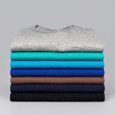 Sale Photo Thumbnail #34: Neatly folded stack of seven crewneck shirts in an assortment of solid colors, including grey knit, teal, cyan, royal blue, brown, navy, and black.