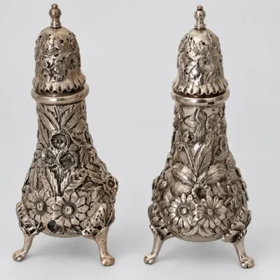 Sale Photo Thumbnail #69: Pair of S. Kirk & Son Sterling silver salt and pepper shakers featuring intricate repoussé floral designs and tripod feet.