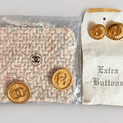 Sale Photo Thumbnail #105: Vintage Chanel extra buttons set featuring gold-tone CC logo buttons with a fabric swatch, alongside additional initial-embossed buttons in paper packaging.