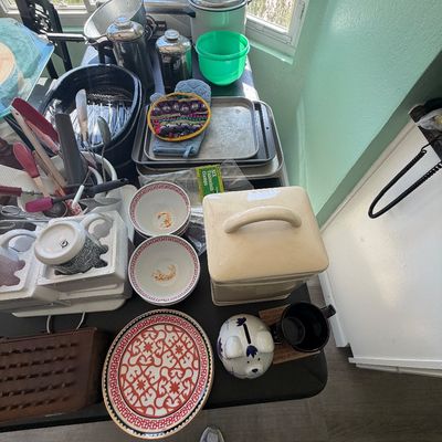 Sale Photo Thumbnail #86: Collection of assorted kitchenware including ceramic bowls and plates, baking sheets, small appliances, metal carafes, and utensils displayed on a folding table.