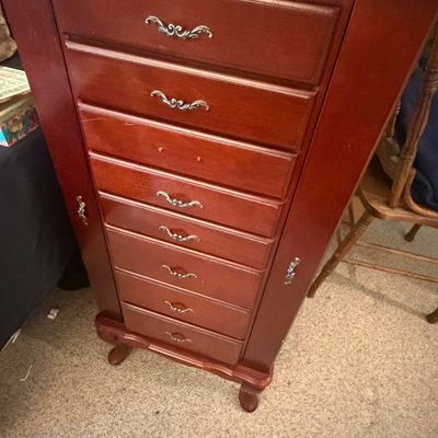 Sale Photo Thumbnail #300: Traditional cherry-finished standing jewelry armoire featuring multiple drawers with ornate metal handles and side flip-out doors.