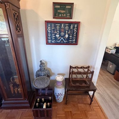 Sale Photo Thumbnail #124: Collection of home decor items including a tall grandfather clock, framed nautical knot display, a terracotta warrior figure, a large Chinese porcelain floor vase, and a wooden wine rack on a side table.