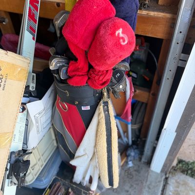 Sale Photo Thumbnail #54: Vintage golf bag packed with various clubs, plush red and navy headcovers, golf gloves, and a towel.