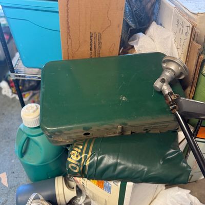 Sale Photo Thumbnail #207: Vintage Coleman green propane stove with a matching Coleman vinyl storage bag, surrounded by camping gear and storage containers.