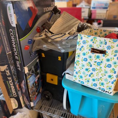 Sale Photo Thumbnail #50: Selection of garage and home goods on a metal shelf, featuring a Wild Sports cornhole game set in box, a rolling toolbox, plastic storage tote, and floral storage box.