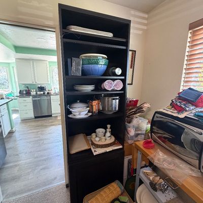 Sale Photo Thumbnail #153: Tall black composite wood bookcase filled with assorted kitchenware and dishware.