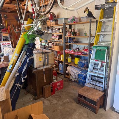 Sale Photo Thumbnail #51: Crowded garage full of household goods, featuring metal shelving units stocked with canned food, a Keller fiberglass stepladder, a step stool, and ceiling-suspended bicycles.