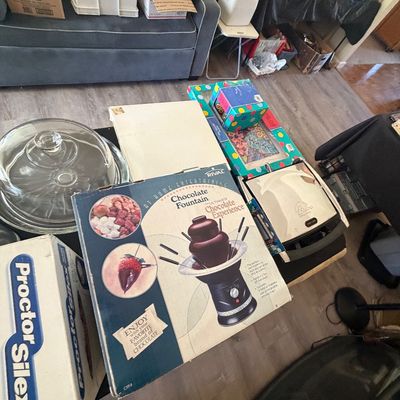 Sale Photo Thumbnail #92: Selection of small kitchen appliances and household items including a Rival Chocolate Fountain in its original box, clear glass cake dome, and boxed electronics.