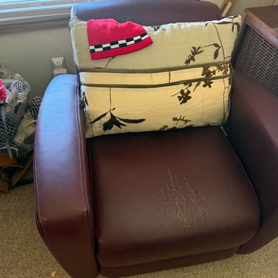 Sale Photo Thumbnail #135: Contemporary burgundy leather armchair with noticeable cracking and wear on the seat cushion, accented with a botanical throw pillow.