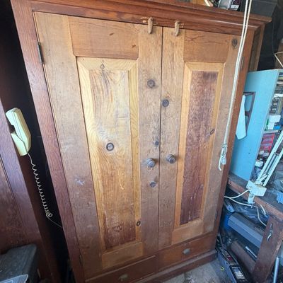 Sale Photo Thumbnail #218: Rustic antique wooden armoire cabinet featuring panel doors, wooden knobs, and bottom drawers, showing surface wear.