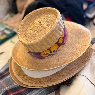 Sale Photo Thumbnail #170: Stack of woven straw sun hats featuring a top hat decorated with a colorful hand-painted floral ribbon band.