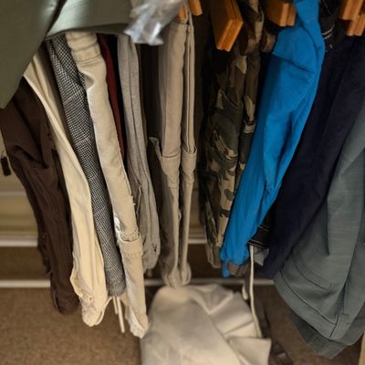 Sale Photo Thumbnail #178: Collection of men's trousers and shorts hanging on a closet rack, including camouflage print, khaki, and bright blue casual pants.