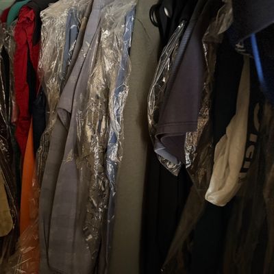 Sale Photo Thumbnail #189: Assorted men's clothing hanging on a rack, including dress shirts and jackets, mostly protected in clear garment bags.