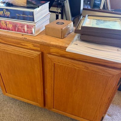 Sale Photo Thumbnail #165: Light oak two-door storage cabinet topped with books, framed artwork, and office supplies.