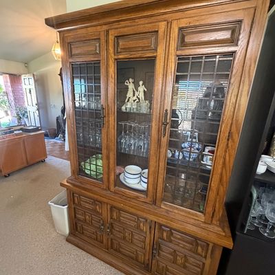 Sale Photo Thumbnail #150: Vintage oak hutch cabinet with leaded glass door panels, geometric carved lower cabinet doors, and display shelves filled with glassware.