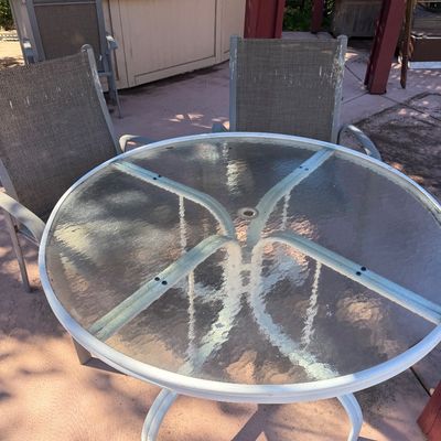 Sale Photo Thumbnail #72: Outdoor patio set featuring a round glass-top table with a white metal frame and matching mesh fabric chairs showing light weathering.