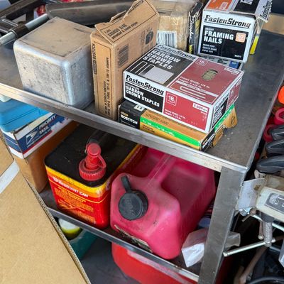 Sale Photo Thumbnail #223: Metal utility cart stocked with assorted hardware supplies, including boxes of FastenStrong framing nails and crown staples, Stanley Bostitch staples, and red gas cans on the lower shelf.