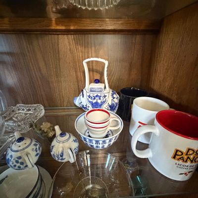 Sale Photo Thumbnail #148: Collection of blue and white Chinese porcelain teapots and small cups arranged alongside novelty coffee mugs on a glass display shelf.