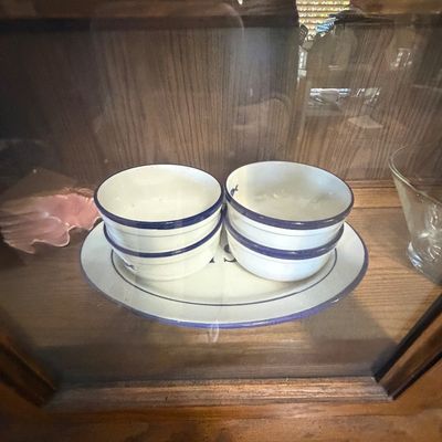 Sale Photo Thumbnail #143: Vintage white enamelware set featuring blue rim accents, including two stacks of small bowls resting on a matching oval platter.