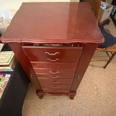 Sale Photo Thumbnail #299: Standing wooden jewelry armoire featuring a cherry finish, multiple drawers with ornate metal handles, and side storage doors.