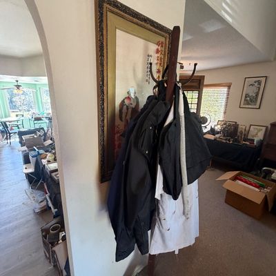 Sale Photo Thumbnail #42: Freestanding dark wood coat rack holding various jackets and bags, positioned next to a large framed Asian art piece.