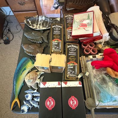 Sale Photo Thumbnail #128: Collection of decorative items, including fish figurines, Jack Daniel's Heritage Series tins, boxed craft kits, and vintage stationery displayed on a table.