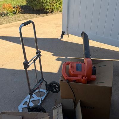 Sale Photo Thumbnail #220: Folding aluminum hand truck alongside an orange electric leaf blower sitting atop cardboard packing boxes outdoors.