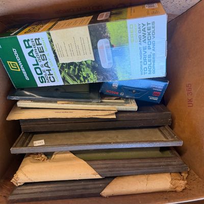 Sale Photo Thumbnail #252: Cardboard box packed with assorted items including vintage picture frames, a Bosch wall scanner, and a boxed Greenwood solar mole and gopher chaser.