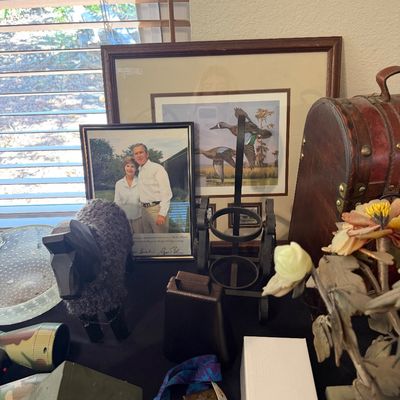 Sale Photo Thumbnail #157: A collection of tabletop items including framed duck art, an autographed framed photograph of George W. and Laura Bush, a small dark sheep figurine, and a metal wine bottle holder.