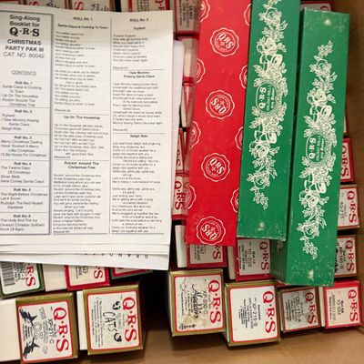 Sale Photo Thumbnail #161: Cardboard box filled with Q-R-S player piano rolls in original boxes, including Christmas and showtune titles, accompanied by a sing-along booklet.