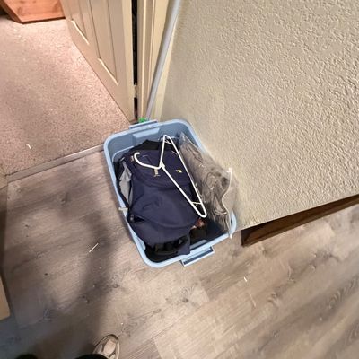 Sale Photo Thumbnail #119: Blue plastic storage tote containing a navy backpack, clothes hanger, and bagged items, shown on a wood-look floor.