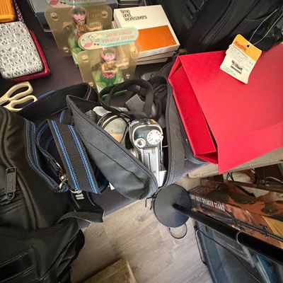 Sale Photo Thumbnail #101: Collection of assorted items including camera gear in a black bag, solar-powered hula dancer novelties, eyewear boxes, and a red Kodak box.