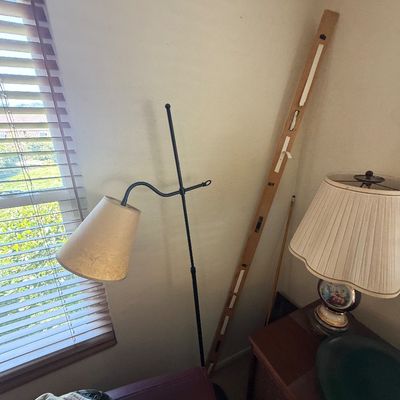Sale Photo Thumbnail #134: Black metal bridge arm floor lamp with a beige fabric shade standing in a room corner beside a vintage table lamp and a long wooden ruler.