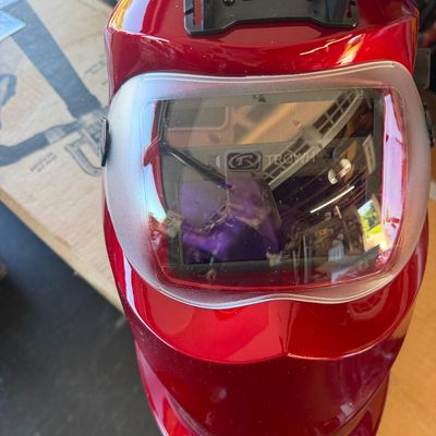 Sale Photo Thumbnail #240: Metallic red auto-darkening welding helmet by TRQWH featuring a clear protective front lens and adjustable top bracket, in good condition.